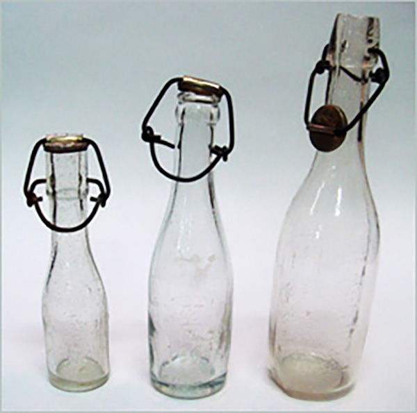 細口ガラスびん（明治～昭和時代）金属製のふたを針金で閉じたタイプ。5勺（約90ML）、1合（約180ML）、2合（約360ML）のタイプがあり、家庭の経済事情などによって選ばれた。（現物は（公財）中田俊男記念財団牛乳博物館に展示されています）